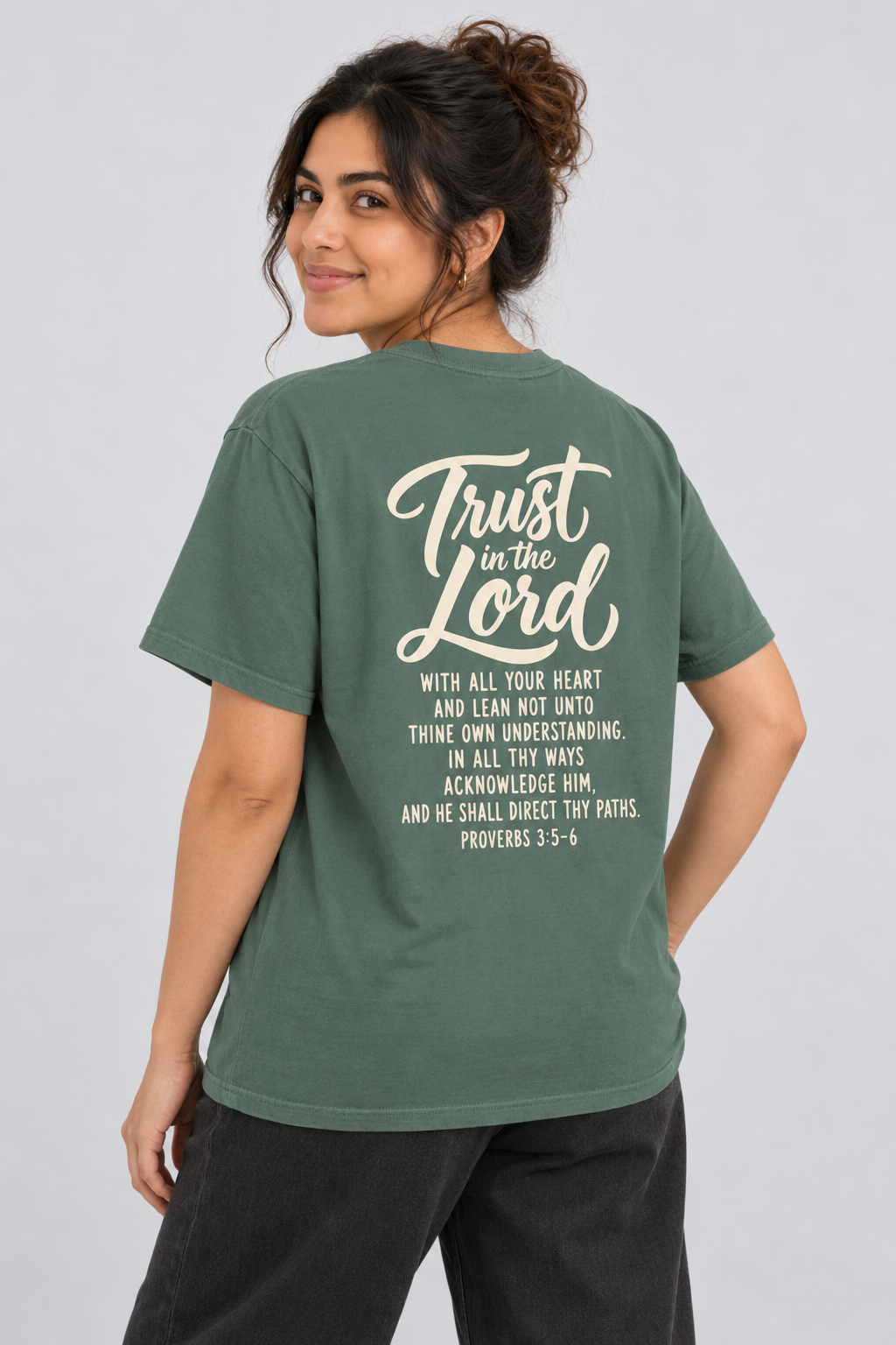 Woman wearing the Blue Spruce Trust In The Lord Tee in a shoulder-turn back pose.