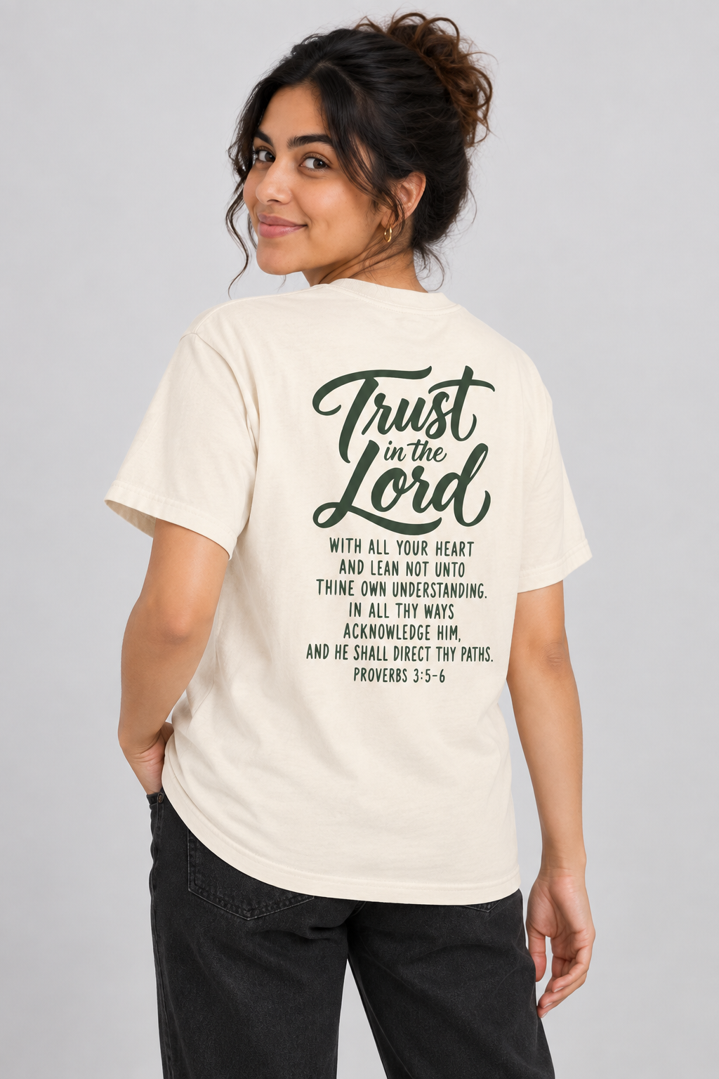 Woman wearing the Ivory Trust In The Lord Tee in a shoulder-turn back pose.