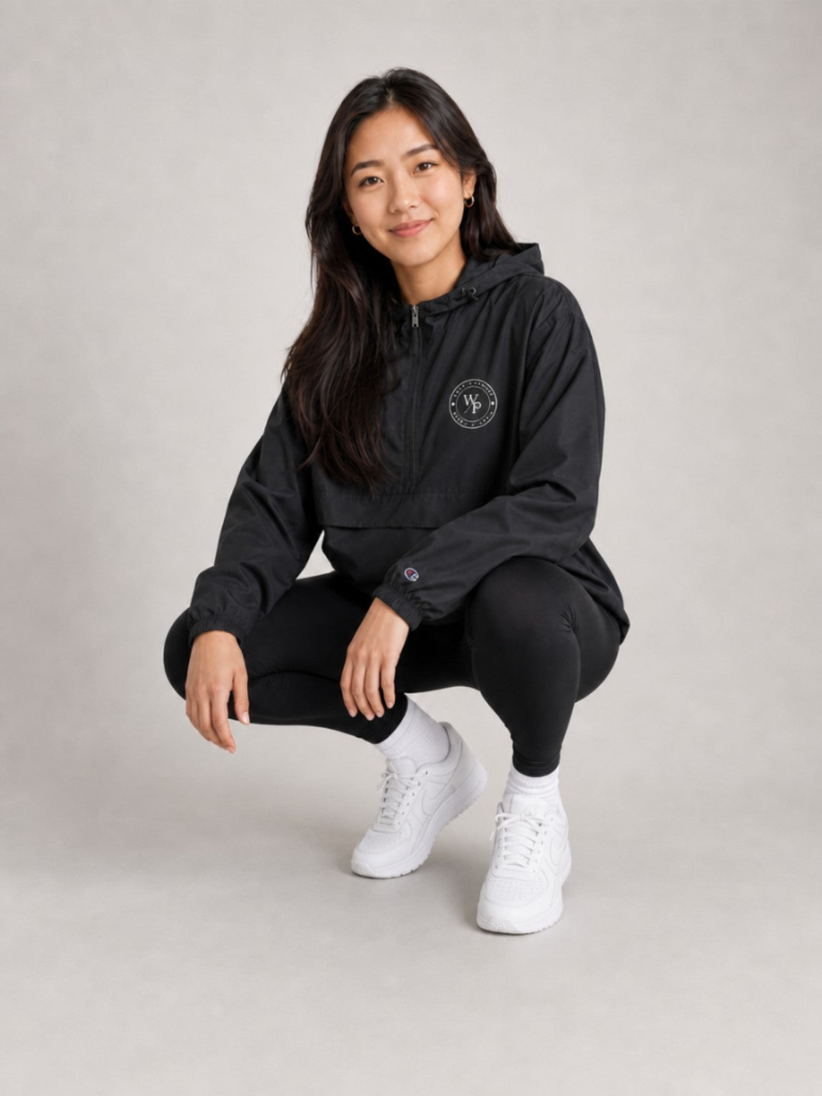 Woman wearing black Worn with Purpose Champion packable anorak, crouching lifestyle view